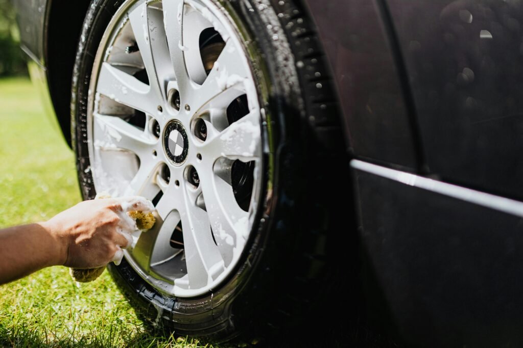 Pessoa lavando a roda de um carro com esponja e sabão em área externa, ilustrando a versatilidade dos produtos da Unilimp em diferentes tipos de limpeza